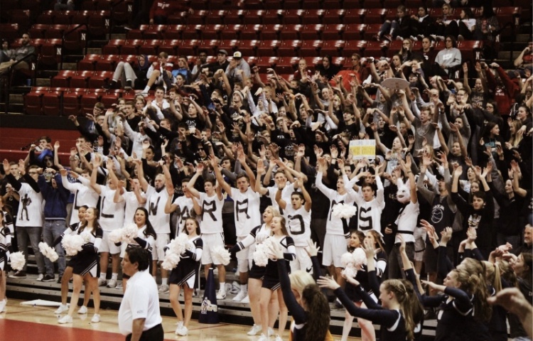 Student section raises their hands in “roof” motion as they celebrate a big block